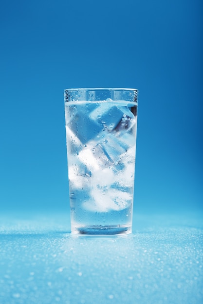 Eiswürfel in einem Glas mit kristallklarem Wasser auf einer blauen Oberfläche