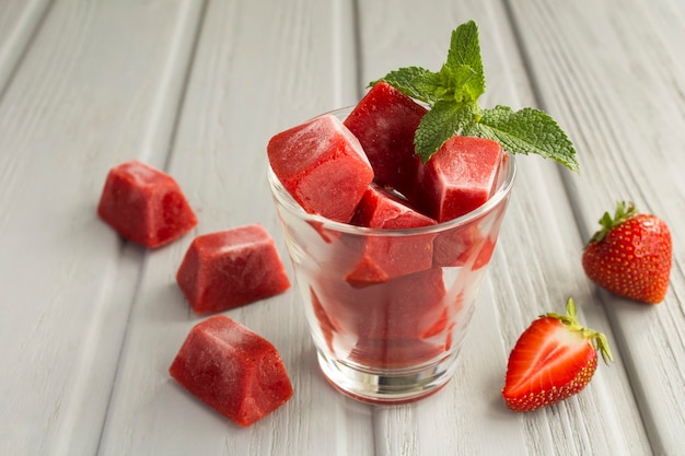 Eiswürfel mit Erdbeere im Glas auf dem grauen Holz