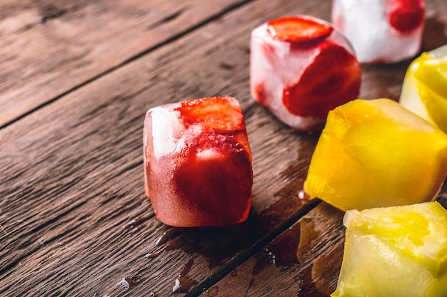 Foto eiswürfel mit früchten auf holztisch. heißes sommerkonzept, nachtisch