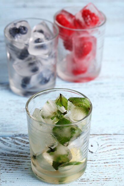 Eiswürfel mit Minzblättern, Himbeere und Blaubeere in Gläsern, auf farbigem hölzernem Hintergrund