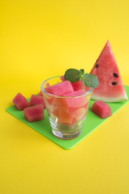 Eiswürfel mit Wassermelone im Trinkglas auf dem grünen Schneidebrett