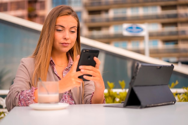 Ejecutiva mujer rubia empresaria desayunando café descafeinado escribiendo un mensaje con el teléfono