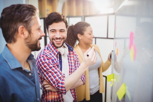 Ejecutivo feliz con colegas de pie junto a la pizarra en la oficina creativa