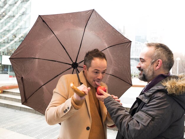 Foto un ejecutivo ofrece una manzana roja a otro que la chupa bajo el paraguas en un día lluvioso