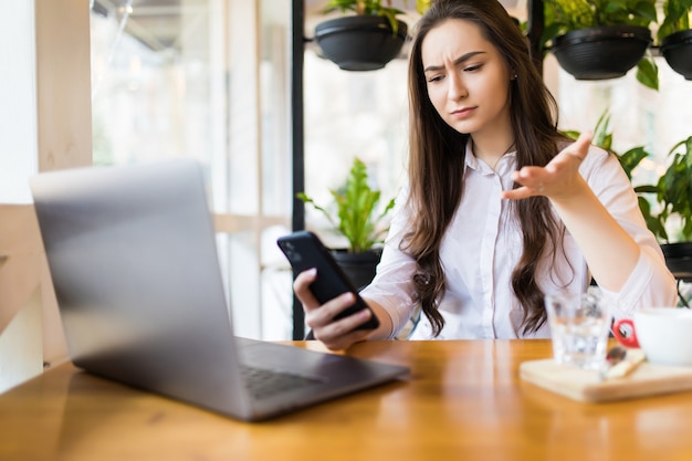 Ejecutivo preocupado hablando por teléfono tratando de resolver problemas con varios dispositivos sentados en un escritorio en la cafetería.