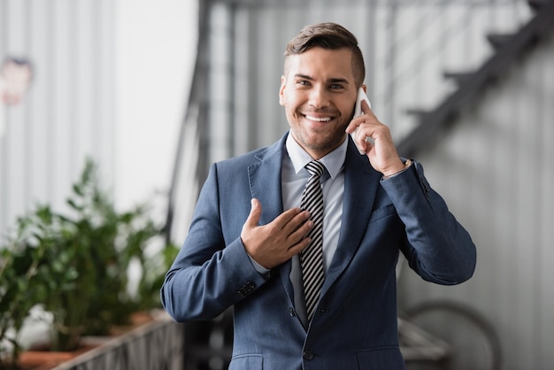 Ejecutivo sonriente mirando a la cámara mientras habla por teléfono móvil en el trabajo con un fondo borroso