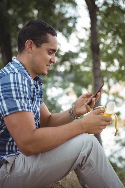 Ejecutivo sonriente mediante teléfono móvil mientras tiene banana