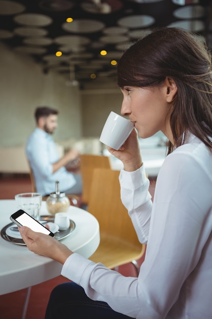 Ejecutivo mediante teléfono móvil mientras toma café en la cafetería