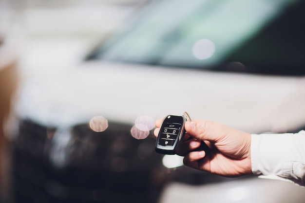 Ejecutivo de ventas que da el primer de la llave del coche con el coche en fondo.