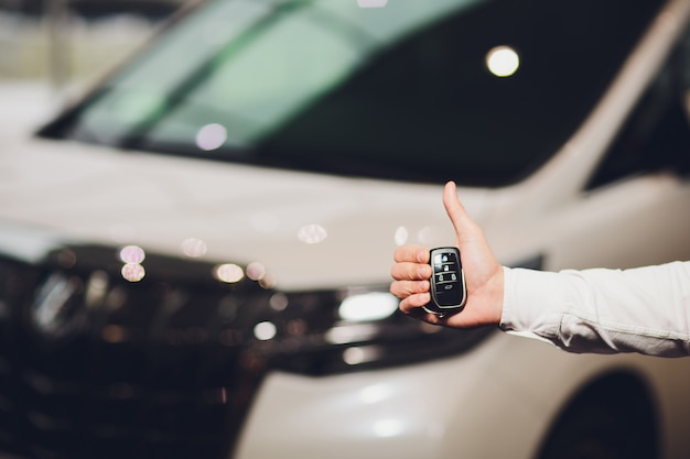 Ejecutivo de ventas que da el primer de la llave del coche con el coche en fondo.