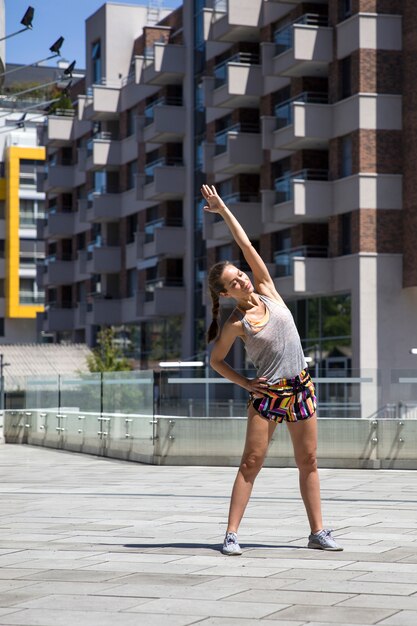 Ejercicio atractivo de la mujer que estira en el ambiente urbano en el día soleado