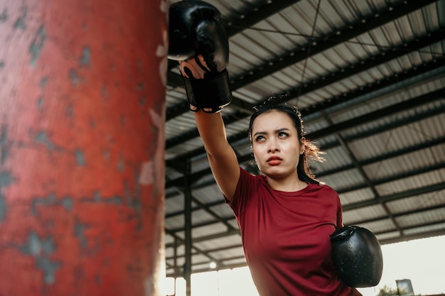 Ejercicio de examen de boxeador de mujer asiática golpeando saco de boxeo en el campo de entrenamiento