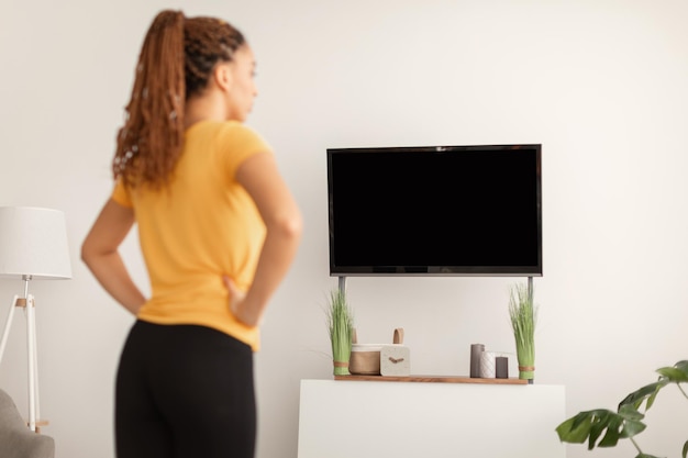 Ejercicio femenino de fitness viendo entrenamiento en televisión vista trasera interior