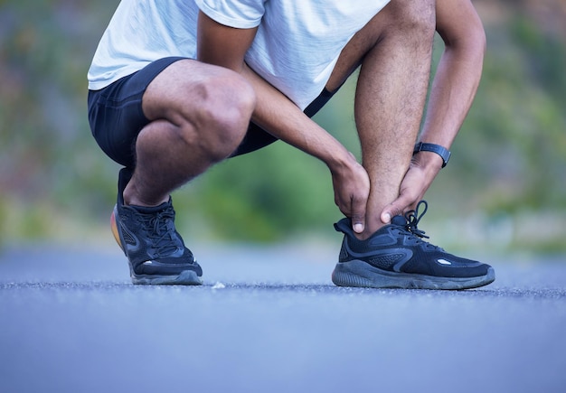 Ejercicio físico y un hombre con lesión en el tobillo al aire libre en entrenamiento o entrenamiento. Primer plano de un atleta o corredor con zapatos para correr y dolor en las piernas, daño muscular o accidente en una carretera para cardio.