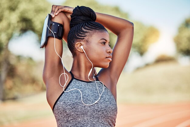 Ejercicio físico y mujer negra escuchando música con auriculares mientras se estira al aire libre para hacer ejercicio y correr Mujer en la naturaleza para cardio con podcast para motivación de rendimiento