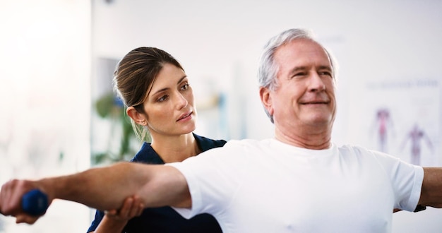 Ejercicio de fisioterapia y fisioterapeuta con un anciano ayudándolo a sanar en una clínica de rehabilitación Bienestar de la salud y un anciano haciendo ejercicio con pesas en clase de fisioterapia