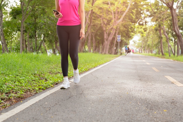 Ejercicio de fitness mujer caminando por el sendero del parque con la mano que sostiene el teléfono celular.