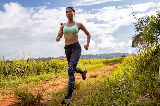 Ejercicio joven asiático de la mujer de la aptitud que corre en el rastro del bosque.