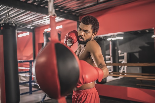 Ejercicio. Kickboxer afroamericano haciendo ejercicio en un gimnasio y mirando concentrado