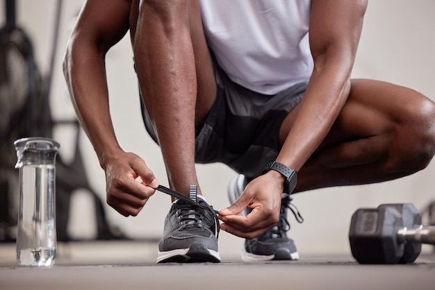 Ejercicio de manos y atar zapatos en el gimnasio para comenzar a entrenar o practicar ejercicio Salud deportiva y hombre negro o atleta atando zapatillas para prepararse para hacer ejercicio de carrera o cardio para el bienestar