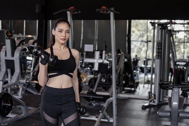 Ejercicio de mujeres sexy asiáticas con pesas en el gimnasio con espacio de copia. Linda mujer con mancuernas de elevación. Muchacha tailandesa que sostiene la pesa de gimnasia en el fondo del gimnasio. Concepto de ejercicio en el gimnasio.