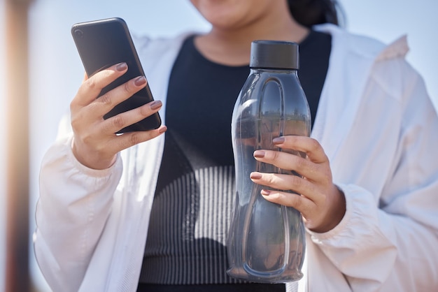 Ejercicio de teléfono y agua para mujeres que usan la aplicación de fitness para verificar los pasos de progreso y la salud mientras se está al aire libre para hacer ejercicio, correr y entrenar Corredor atleta con botella y teléfono inteligente para redes sociales