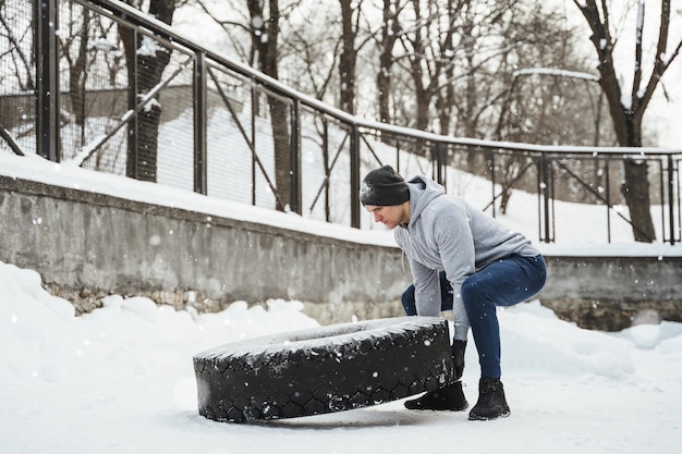 Ejercicio de volteo de llantas. Deportista fuerte durante su entrenamiento de entrenamiento cruzado durante el frío y nevado día de invierno.