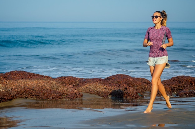 Ejercicios cardiovasculares de joven y bella mujer calentar trotar en la playa, cuerpo delgado de fitness, vida sana