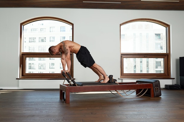 Ejercicios de entrenamiento de reformador de Pilates hombre en el gimnasio interior