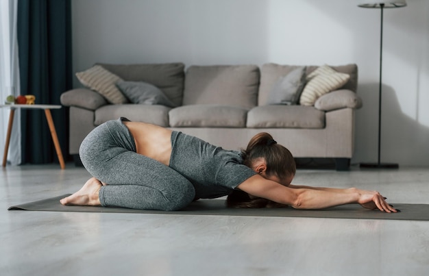 Ejercicios de estiramiento Mujer joven con cuerpo delgado y ropa de yoga está en casa