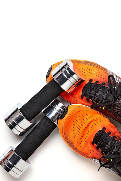Ejercicios de fitness en casa Pesa pesada de metal cayó sobre la pierna en zapatillas naranjas aislado sobre fondo blanco.