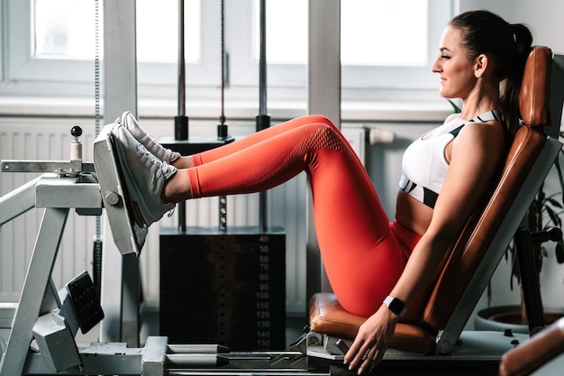 Ejercitar las piernas en la máquina en el gimnasio, instructora de fitness femenino