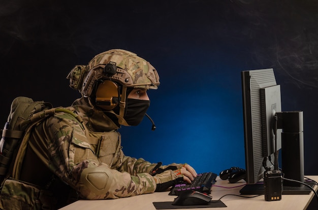 El ejército en uniforme sentado frente a una computadora lleva a cabo una guerra cibernética