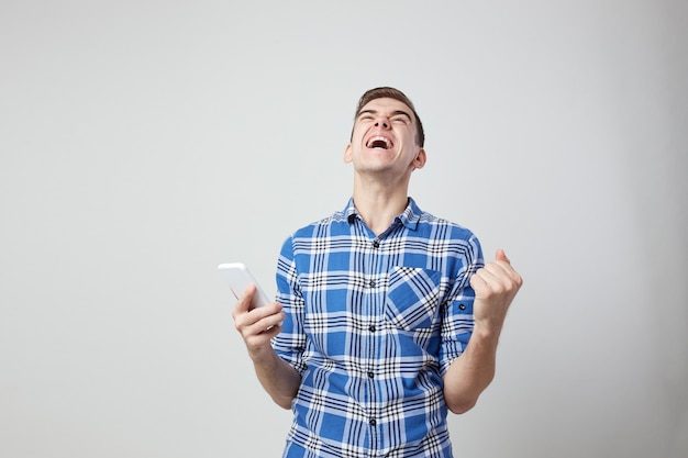 Ekstatischer, energiegeladener Kerl in einem karierten Hemd hält das Handy in der Hand