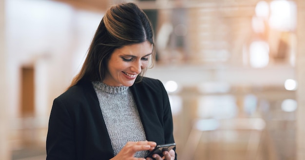 Ela adora receber feedback positivo de sua equipe Foto recortada de uma jovem empresária atraente sorrindo enquanto usa smartphone em um local de trabalho moderno