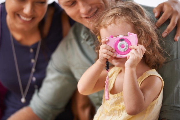 Ela começou a praticar sua fotografia para a viagem Uma garotinha brincando com uma câmera enquanto se senta com seus pais