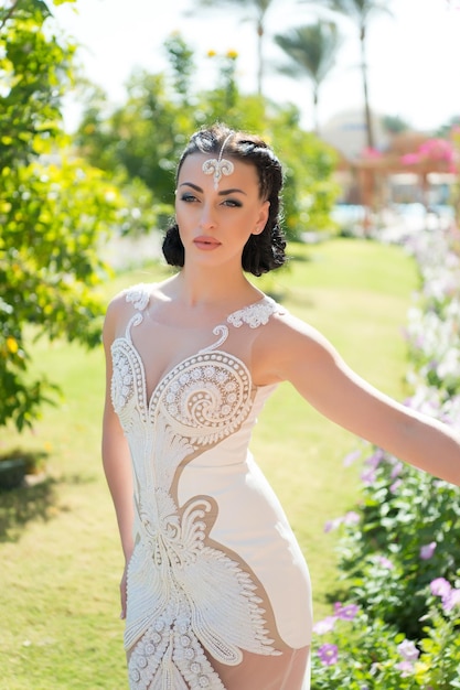 Ela é perfeita garota atraente acessório de vestido de luxo senhora com roupa de luxo anda fundo de jardim exótico mulher maquiagem penteado usa vestido elegante e justo com bordados e pérolas