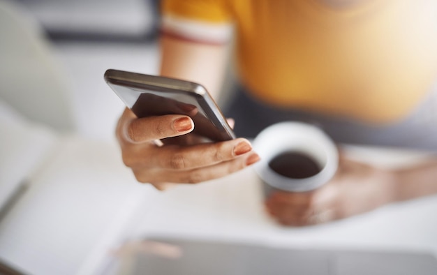 Ela está com o celular e o café prontos para o dia captura de uma designer feminina irreconhecível usando um celular em seu escritório em casa