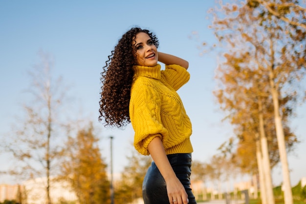 Ela flirta brincando com o cabelo dela jogando-os com a mão de uma beleza brilhante em um suéter amarelo