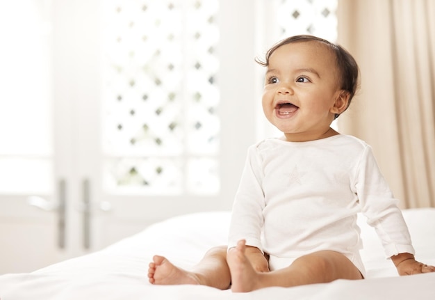 Ela tem o sorriso mais fofo Foto de uma adorável garotinha sentada em uma cama