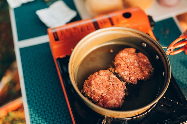 Foto elaboración de alimentos para acampar. hamburguesas en sartén en estufa de fuego turístico. campamento de cocina a la orilla del lago.