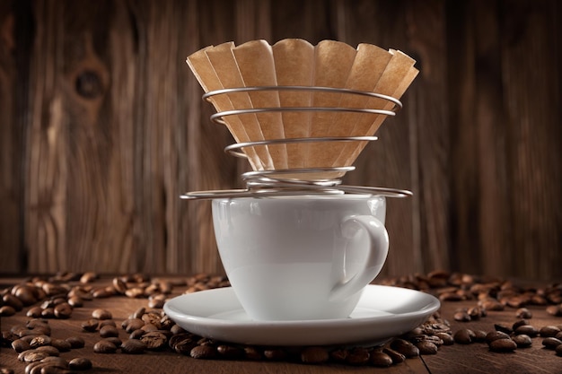 Elaboración alternativa de café. Portafiltros de papel con cable en taza de café de cerámica blanca. Granos De Café Sobre Fondo De Madera Vintage.