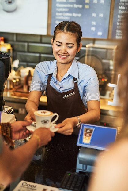 Elaborado con cuidado Foto de un joven barista feliz trabajando detrás de la caja registradora en una cafetería