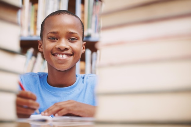 Ele adora bater nos livros Um menino afro-americano cercado por livros na biblioteca