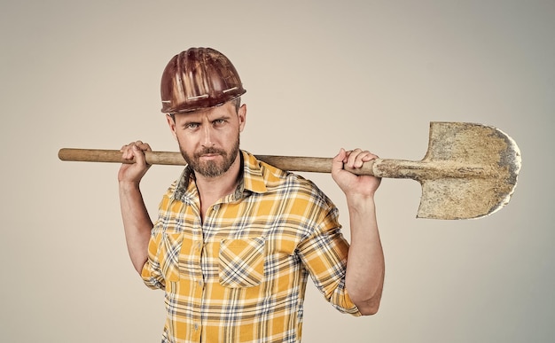 Ele ama seu trabalho construtor maduro em camisa homem com barba no canteiro de obras trabalhador de construção bonito em capacete duro cara do dia do trabalho usar capacete de segurança segurar engenheiro de pá no trabalho estilo de vida masculino