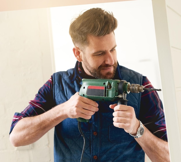 Foto ele é o homem certo para o trabalho foto de um jovem e bonito faz-tudo usando uma furadeira elétrica para fazer bricolage