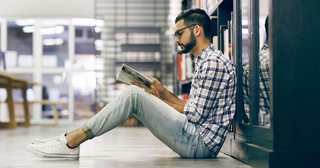 Ele encontrou um lugar tranquilo para estudar Foto de corpo inteiro de uma bela e jovem universidade lendo um livro enquanto está sentado no chão da biblioteca