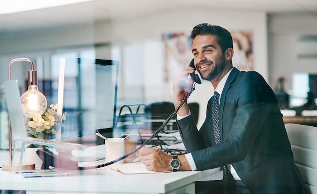 Ele está sempre pronto para receber chamadas de negócios Foto de um jovem empresário alegre fazendo uma ligação enquanto está sentado dentro do escritório