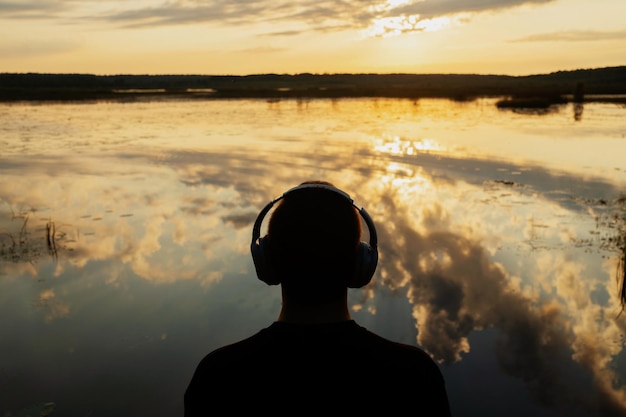 Ele fica de costas olhando o pôr do sol no lago A pessoa ouve um audiolivro Calma
