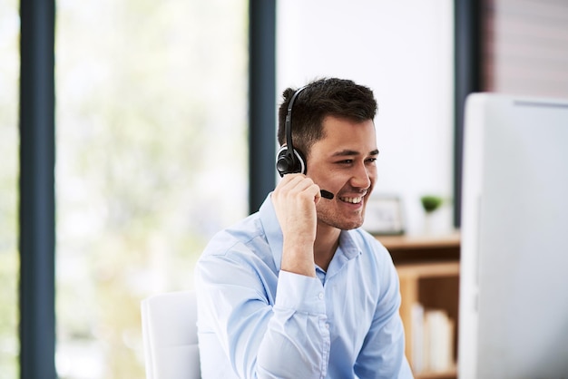 Ele sabe como manter a atenção de seus clientes Foto de um jovem feliz usando um fone de ouvido e um computador no trabalho